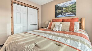 A bedroom with a large bed, a wooden headboard, a painting of a mountain landscape, and a double door.