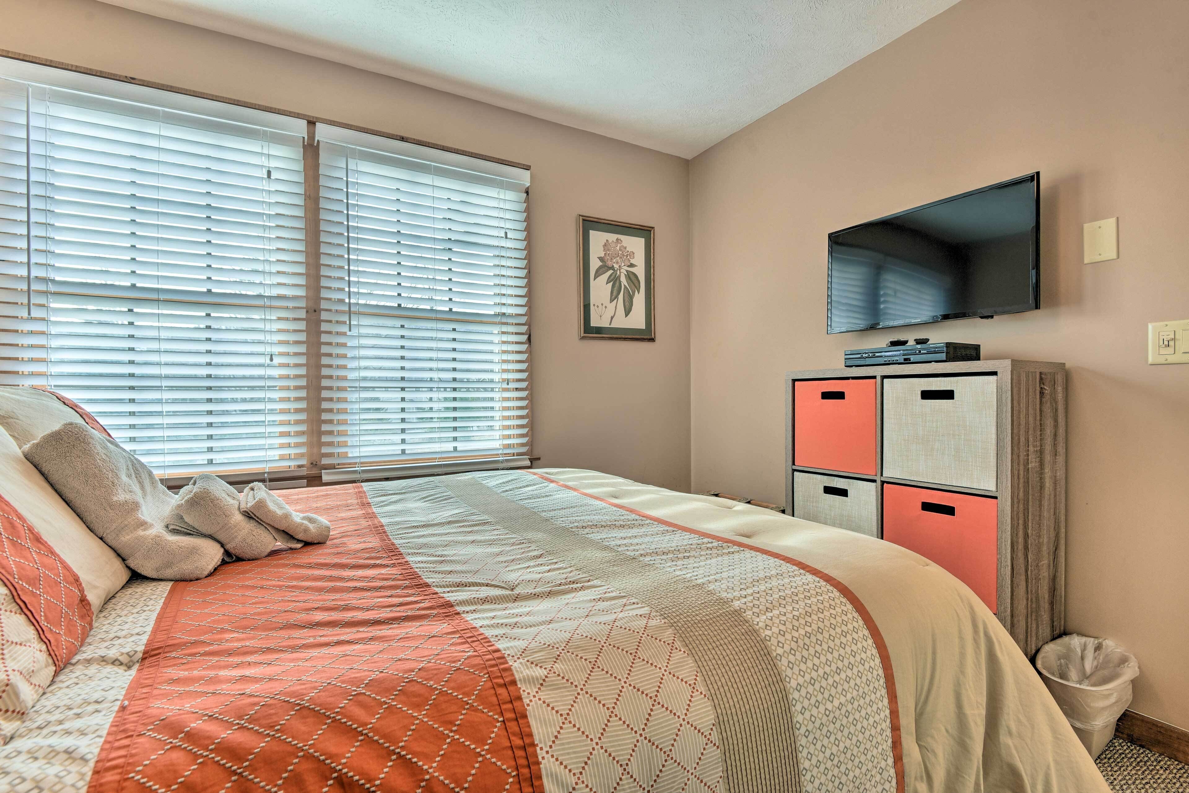 A bedroom with a bed, a TV, a window with blinds, and a dresser with drawers.