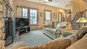 A living room with a stone fireplace, a flat-screen TV, a sofa, and a ceiling fan.