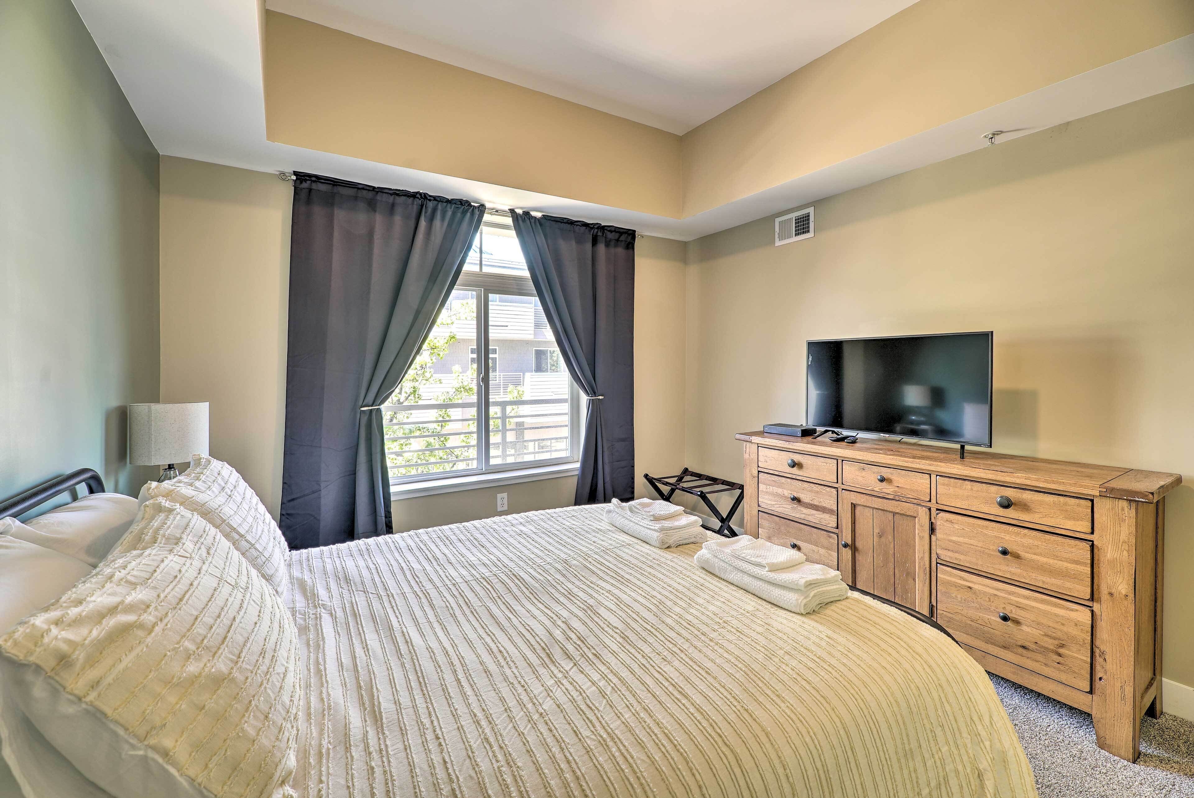 Una habitación de hotel con una cama grande, un aparador de madera, un televisor y una ventana con cortinas.