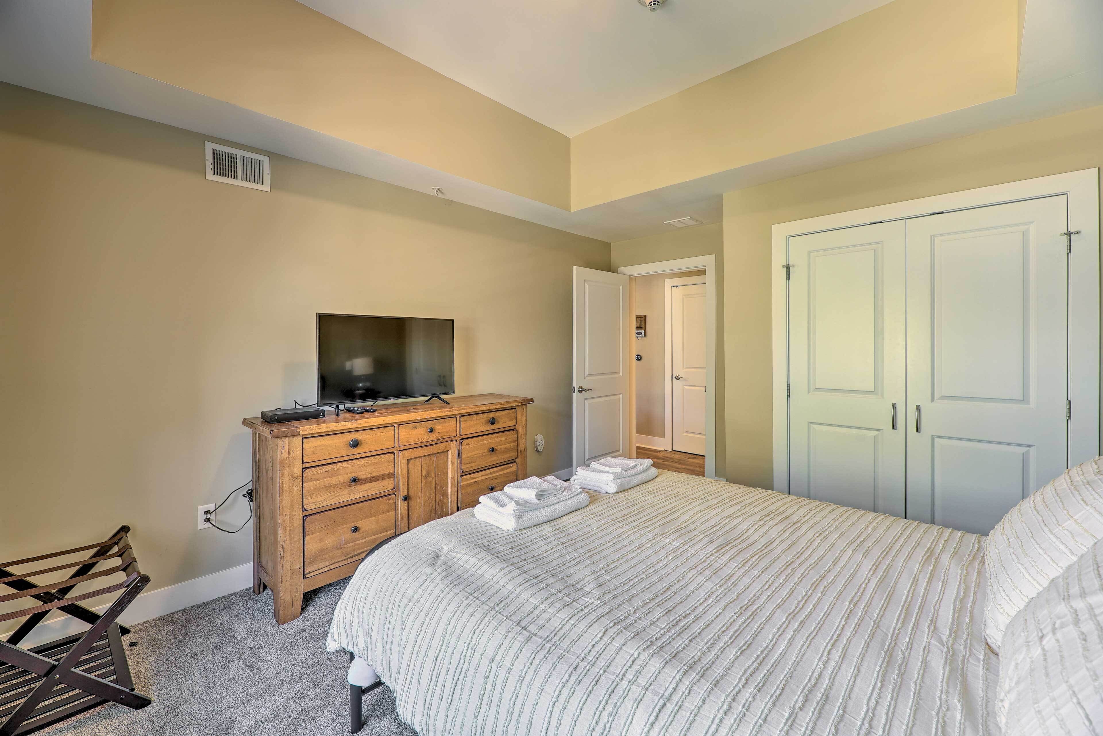 A bedroom with a bed, a wooden dresser, a television, and a door.