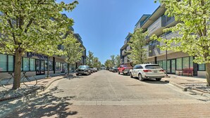 Una calle bordeada de edificios modernos, coches aparcados y árboles.