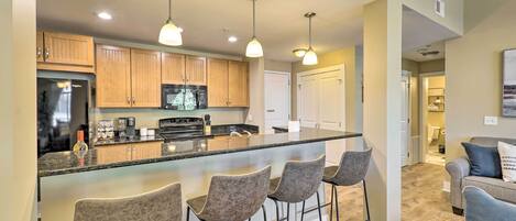 A modern kitchen with wooden cabinets, a black refrigerator, a microwave, and a large island with bar stools.
