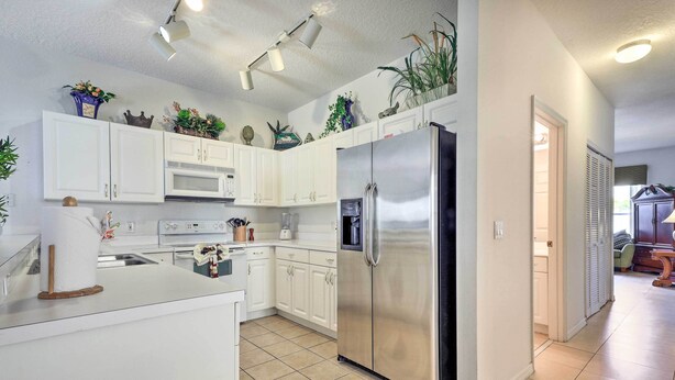 A modern kitchen with white cabinets, a stainless steel refrigerator, and various decorative items on the shelves.
