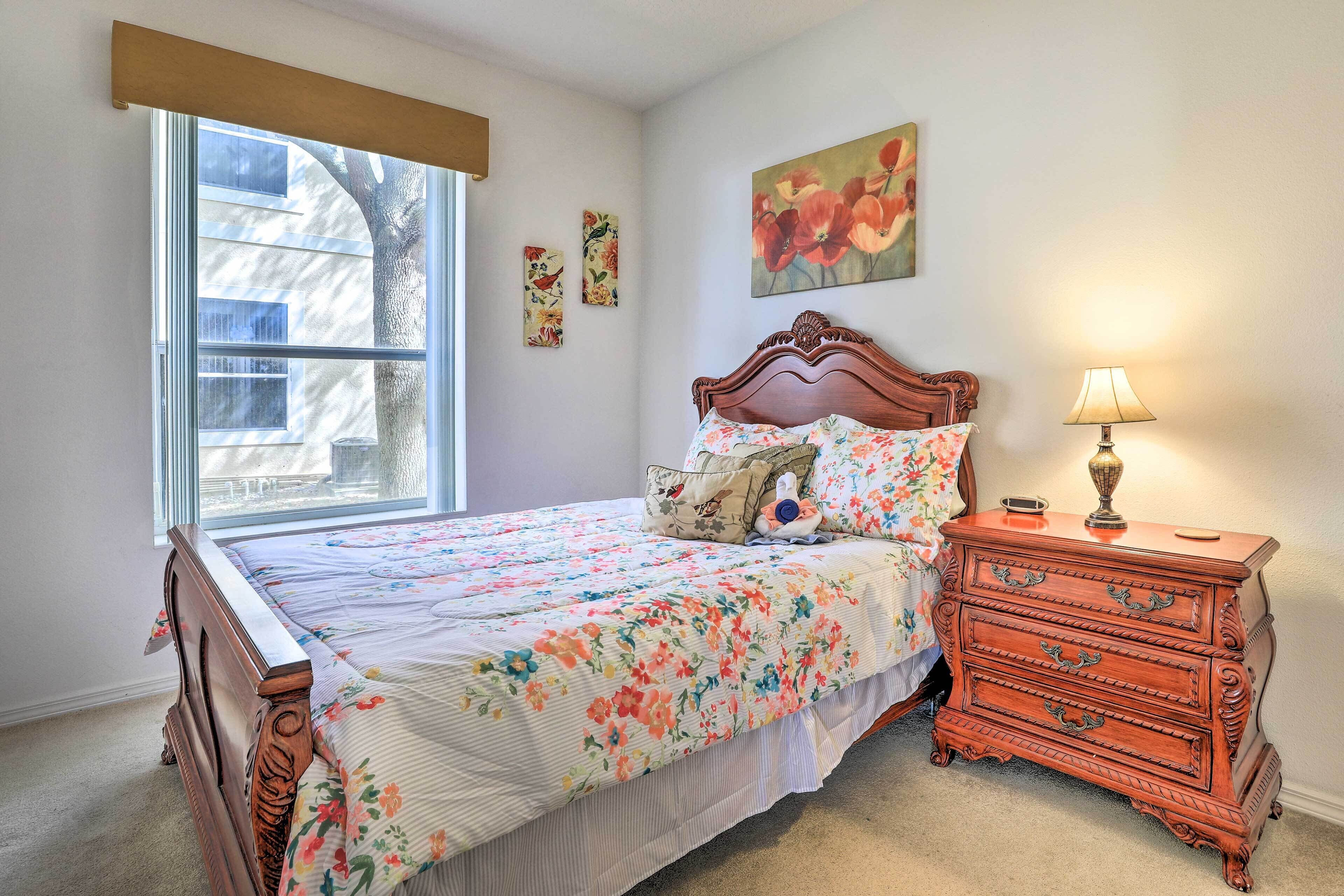 A bedroom with a large window, a wooden dresser, and a floral bedspread.