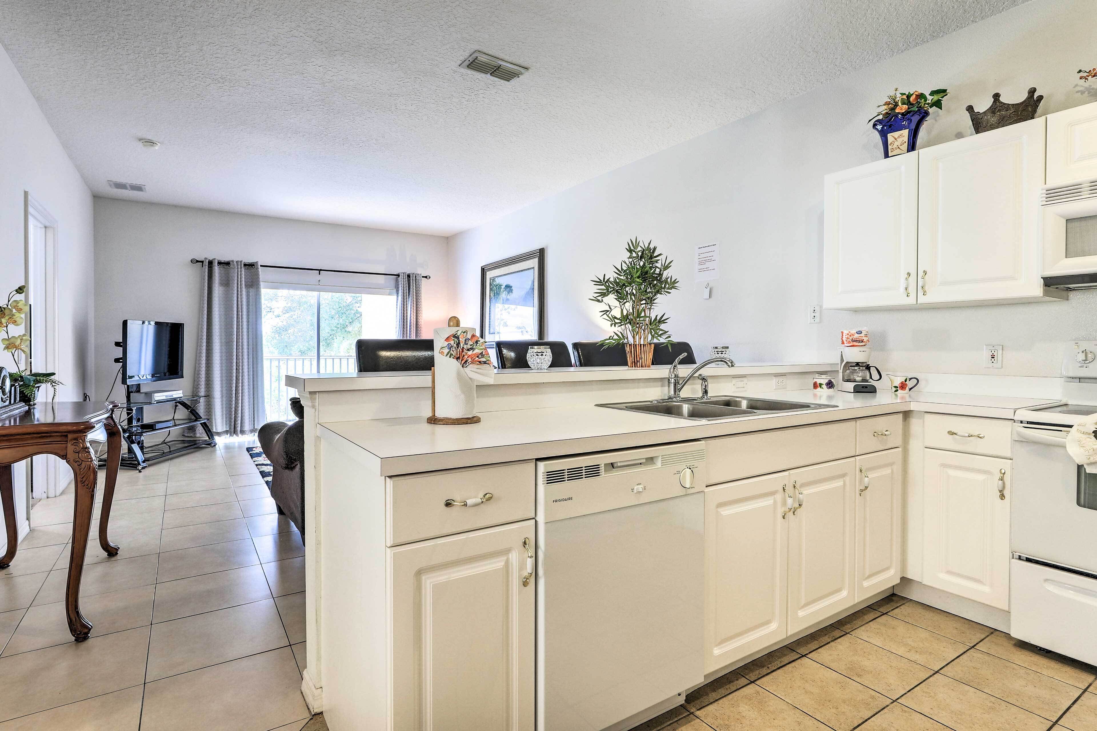 A modern kitchen with white cabinetry, a central island with a sink, and a dining area with a sofa and TV.