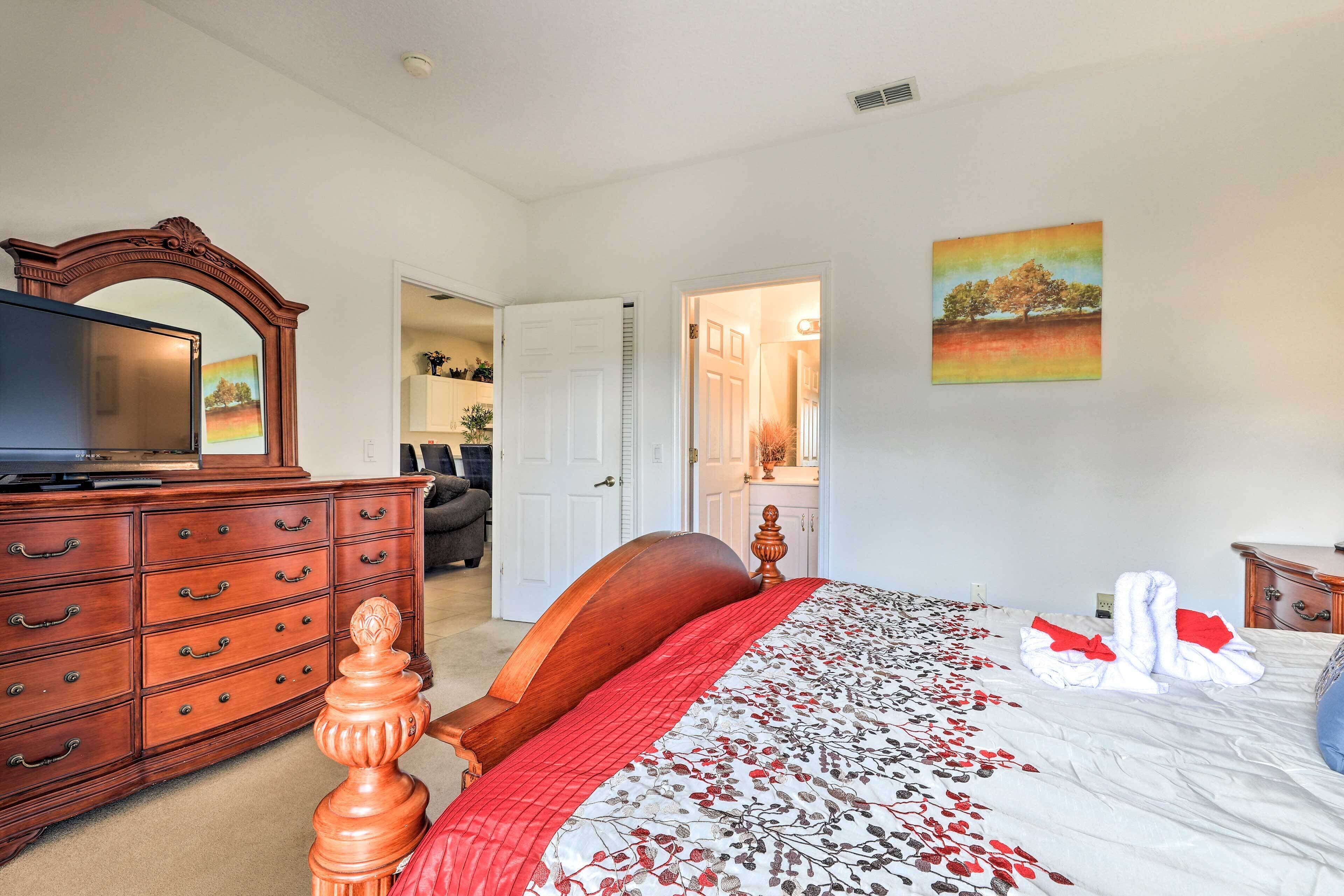 A bedroom with a wooden dresser, a bed with a floral comforter, a painting on the wall, and a mirror above the dresser.