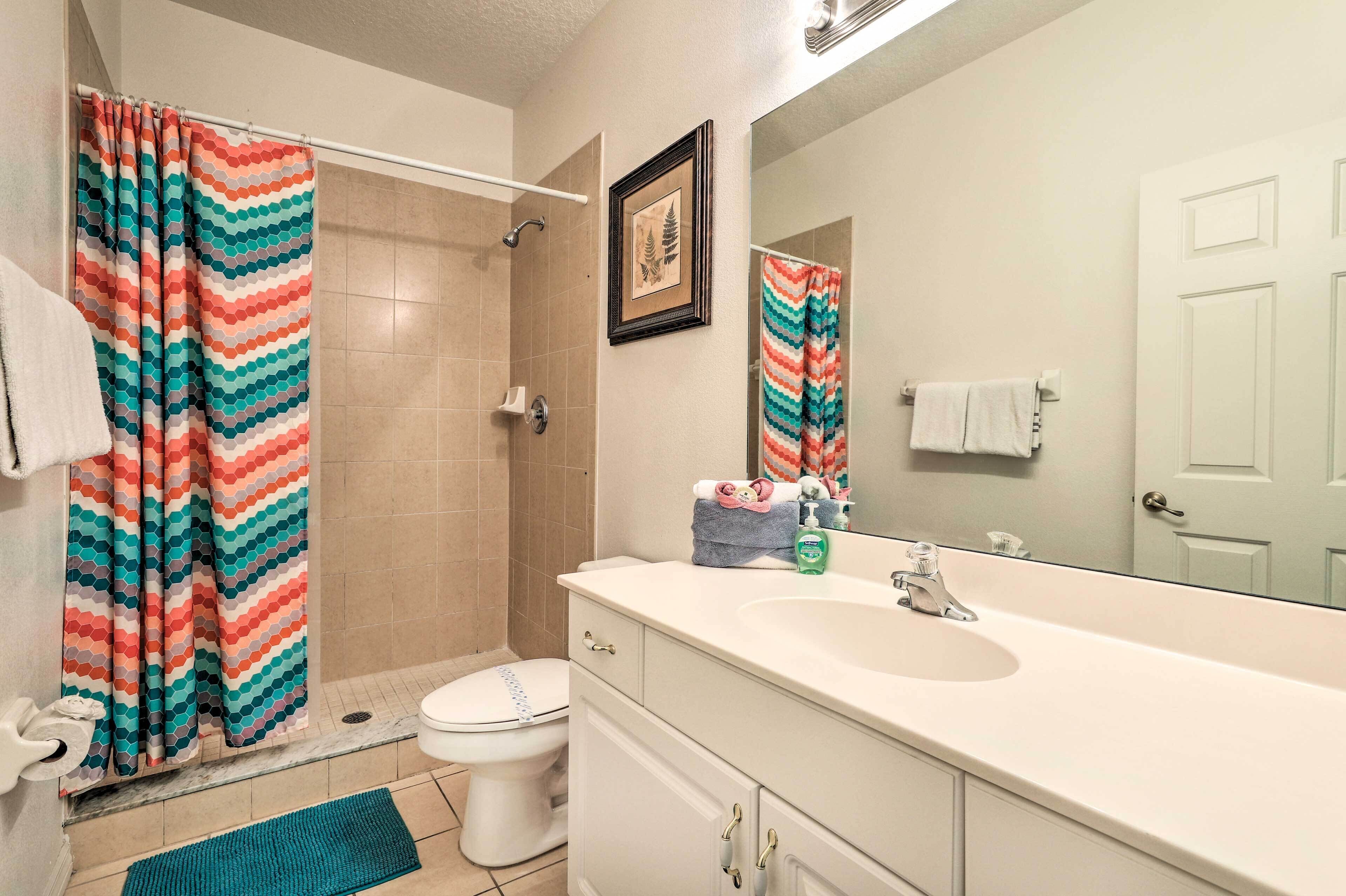 A bathroom with a shower, toilet, sink, and a mirror.