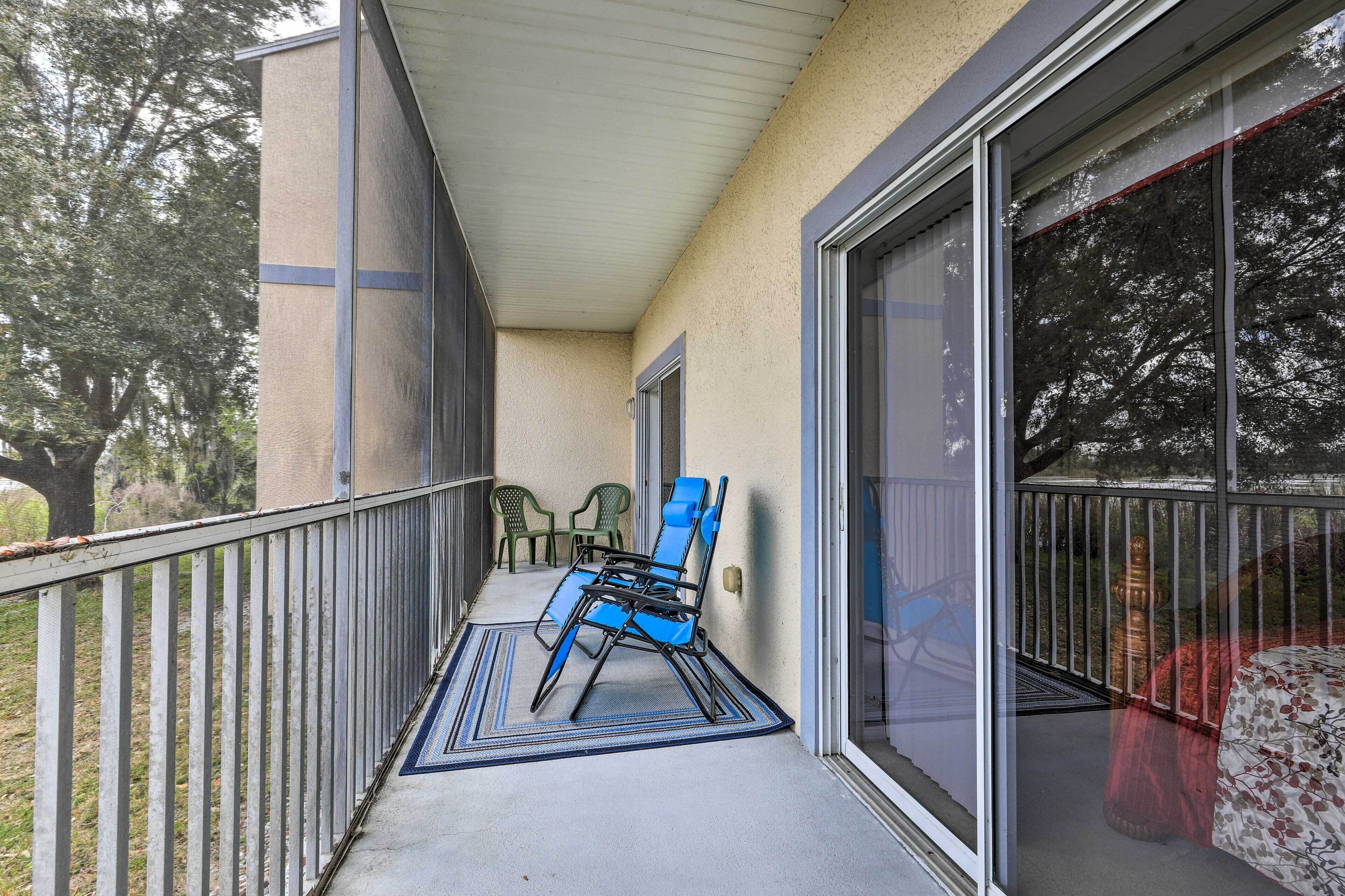 A covered balcony with a blue chair, a green chair, and a small table.
