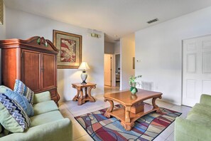 A living room with a sofa, a wooden cabinet, a table, and a rug. - Kissimmee Condo w/ Resort Perks - 5 Mi to Disney! (Kissimmee)