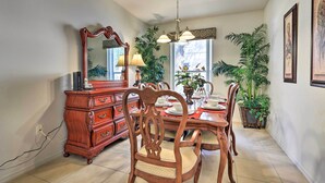 A dining area with a wooden dining table, chairs, a chandelier, a mirror, and potted plants.