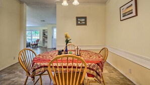 A dining area with a round table, four wooden chairs, a chandelier, and a vase with flowers.