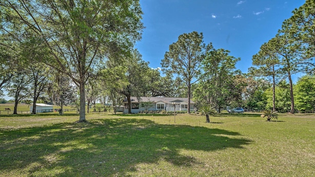 A residential property with a large lawn, several trees, and a house in the background.