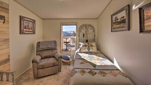 Un dormitorio con cama, una silla, una ventana con vistas y cuadros en la pared.