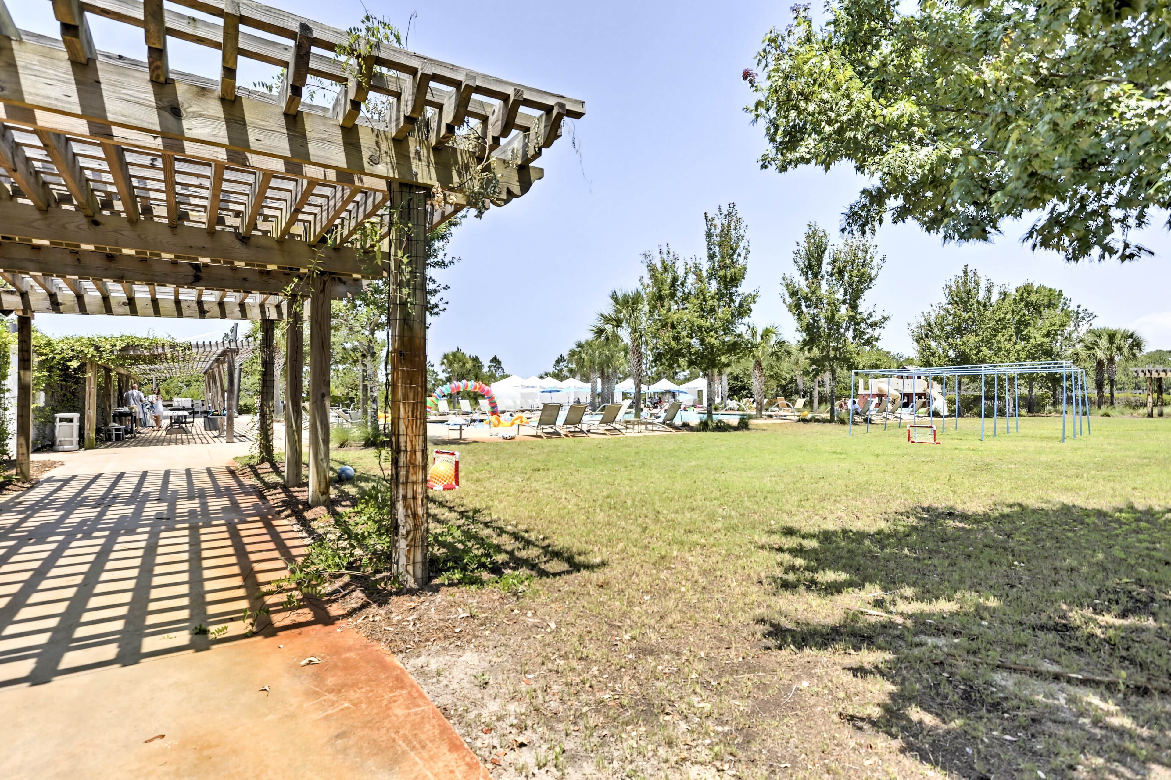 A covered outdoor area with a wooden pergola, a grassy lawn, and a playground with swings and slides.