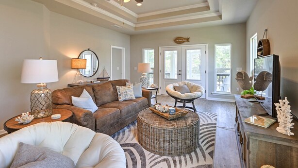A spacious living room with a brown leather sofa, a white armchair, a round wicker ottoman, and a large mirror. - Port St Joe Beach House w/ Pool Access! (Port St. Joe)