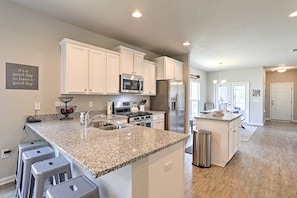 A modern kitchen with white cabinets, granite countertops, stainless steel appliances, and a central island with stools. - Port St Joe Beach House w/ Pool Access! (Port St. Joe)
