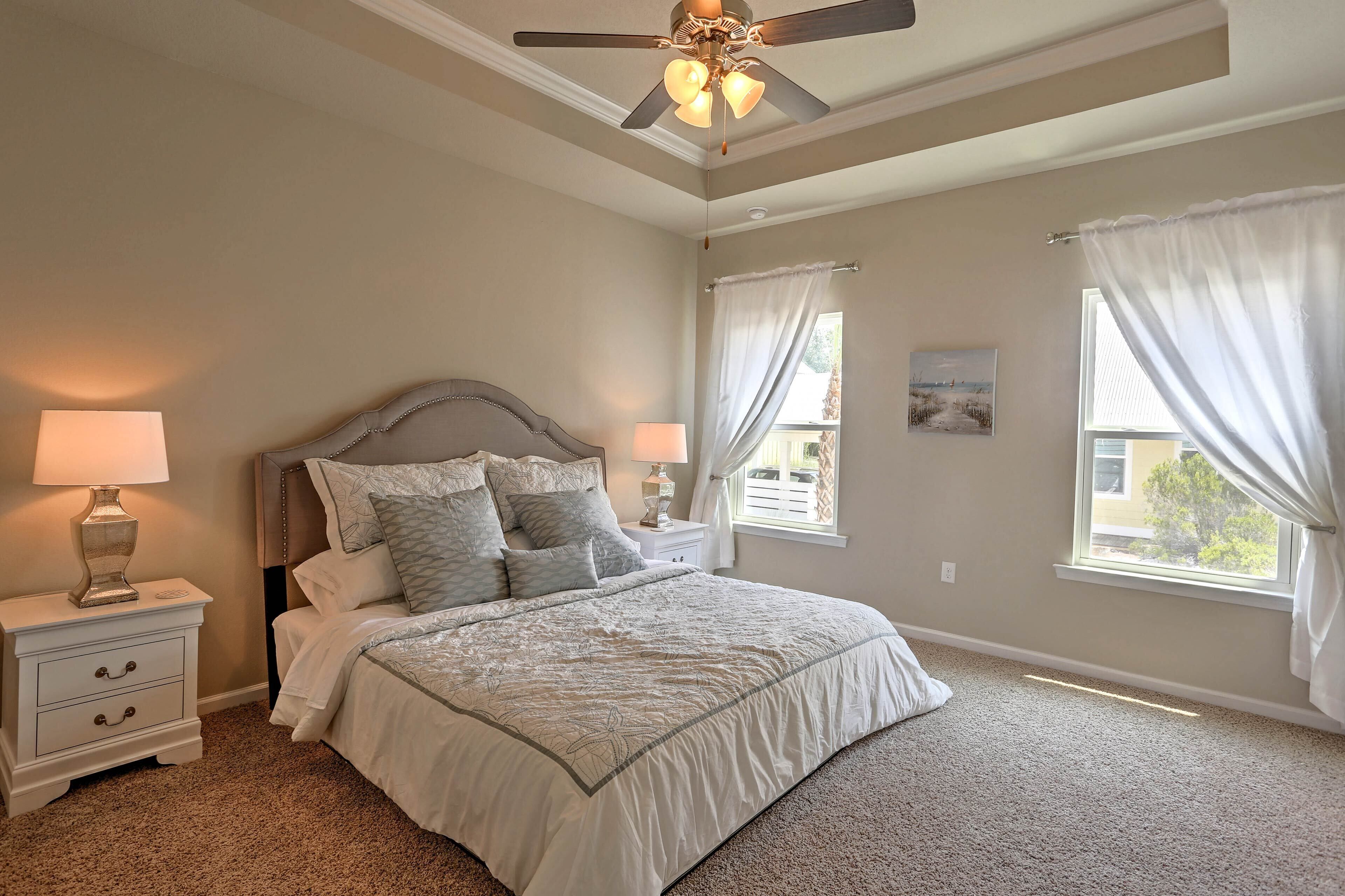 A bedroom with a bed, nightstands, a ceiling fan, and windows with curtains.