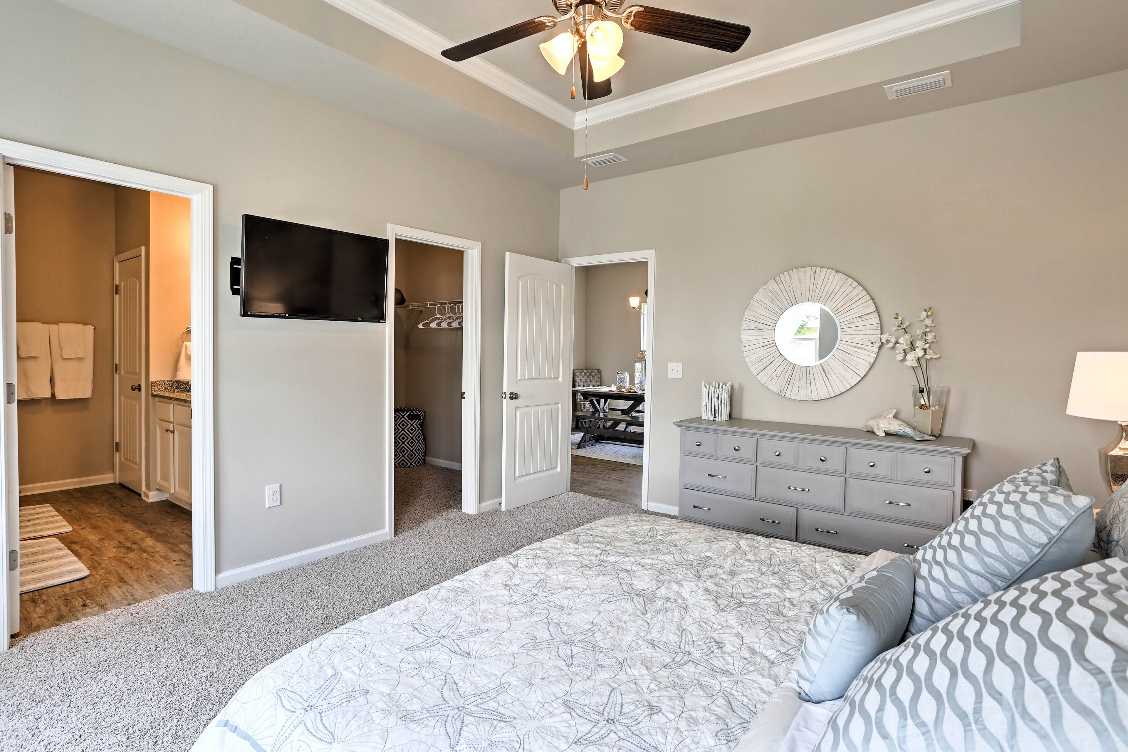 A bedroom with a large bed, a dresser, a TV, and a ceiling fan.