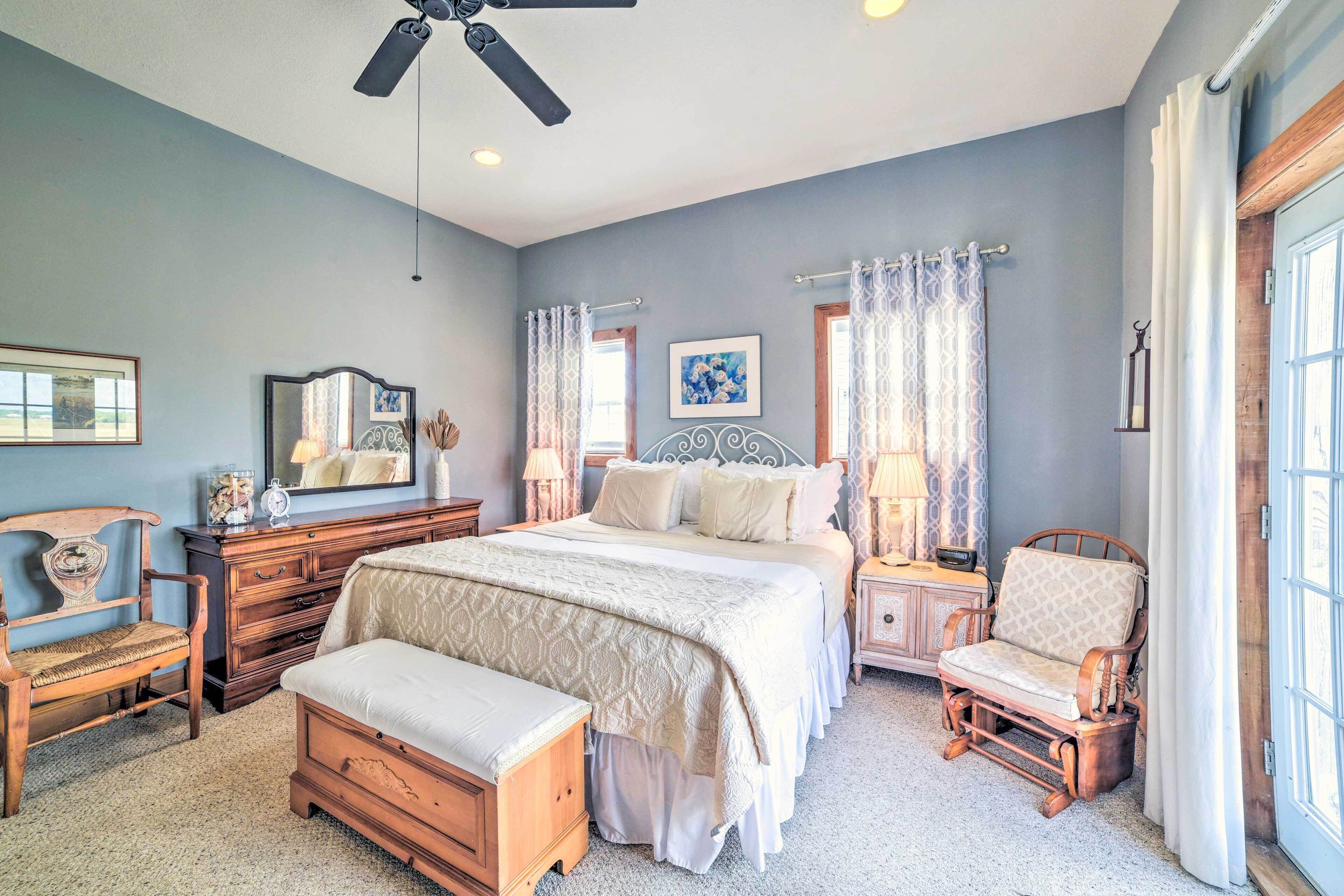 A bedroom with a large bed, a wooden chair, a nightstand, a dresser, and a ceiling fan.