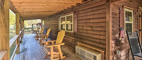 A log cabin with a porch, wooden chairs, and a view of the outdoors.
