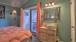 Un dormitorio con cama, un baño con lavamanos y espejo, y un cerramiento de vidrio corredizo que da a otra habitación.