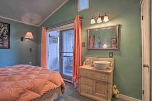 Un dormitorio con cama, un baño con lavamanos y espejo, y un cerramiento de vidrio corredizo que da a otra habitación.