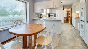 A modern kitchen with white cabinets, a wooden dining table, and a large window. - Gassville Home 3 Mi to White River & Trout Fishing (Gassville)