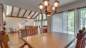 A spacious dining area with a large wooden table and chairs, a chandelier, and large windows offering a view of the outdoors. - Gassville Home 3 Mi to White River & Trout Fishing (Gassville)