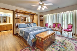 A bedroom with a large bed, a wooden headboard, a nightstand, a dresser, a vanity with a mirror, a ceiling fan, and a window with blinds. - Gassville Home 3 Mi to White River & Trout Fishing (Gassville)