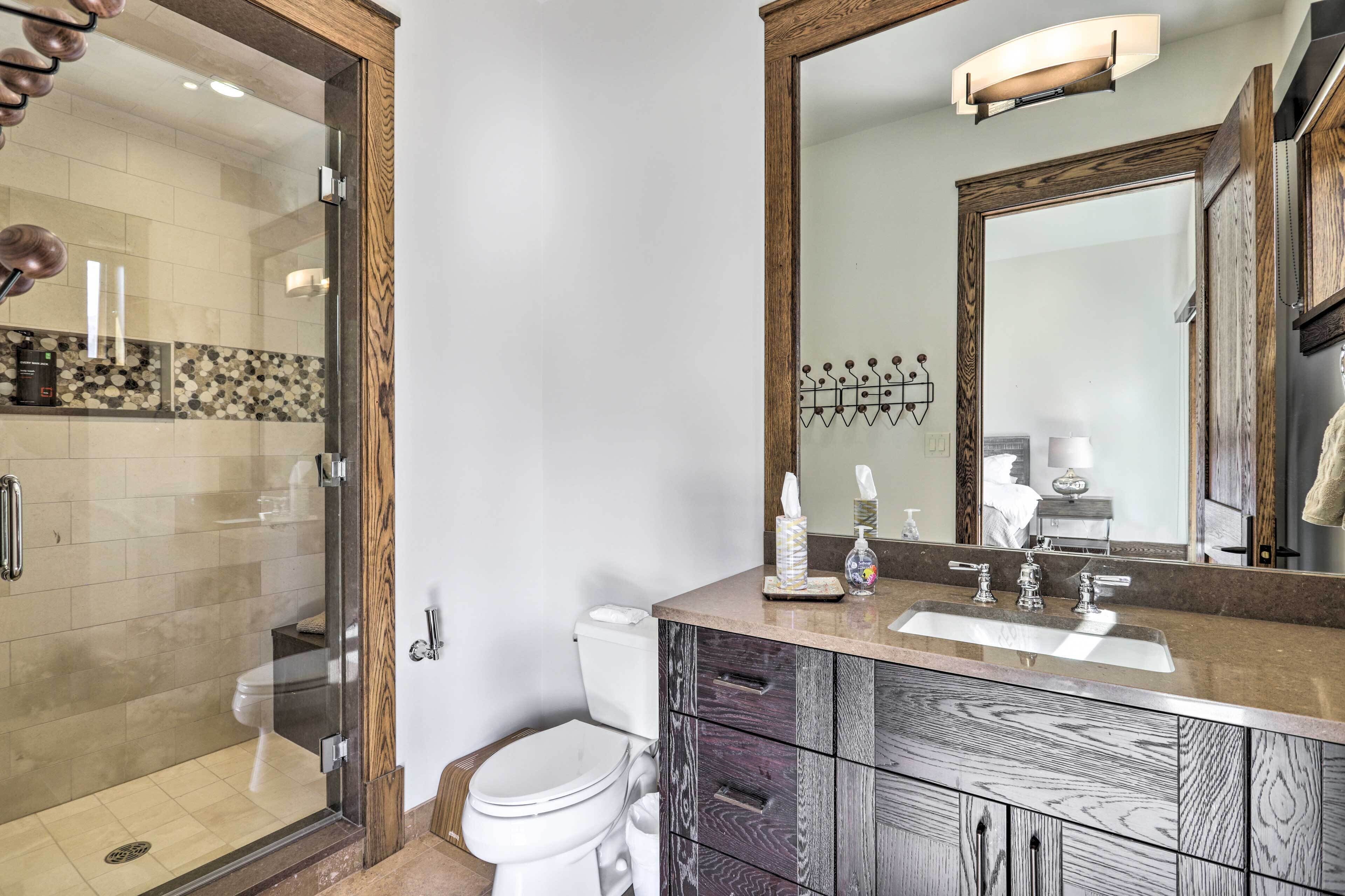 A modern bathroom with a glass shower enclosure, a white toilet, and a vanity with a large mirror and wooden cabinetry.