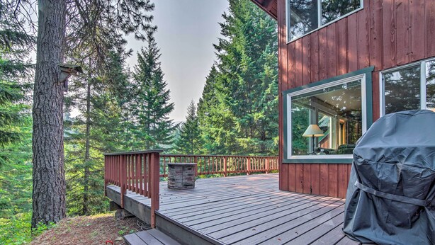 A wooden deck with a grill and a trash can, surrounded by tall trees. - Peace in the Pines: Cle Elum Cabin w/ Trail! (Cle Elum)