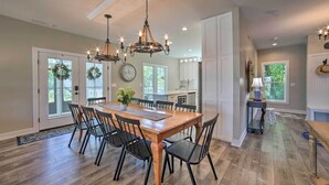 Un vaste espace dédié à la salle à manger, avec une table et des chaises en bois, un lustre, et une vue sur la cuisine et le salon.