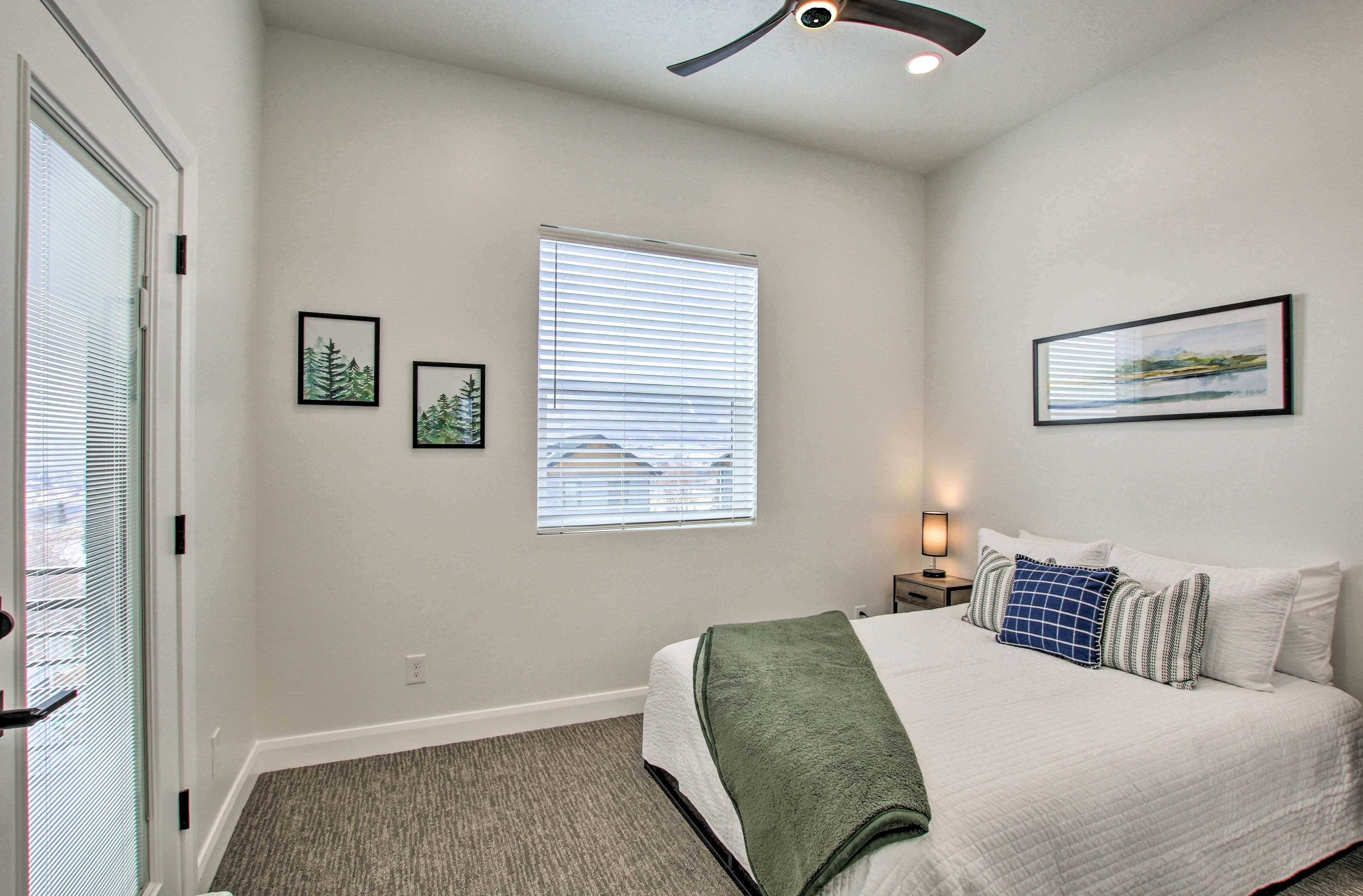 Quarto com cama, janela com persianas, ventilador de teto e obras de arte nas paredes.