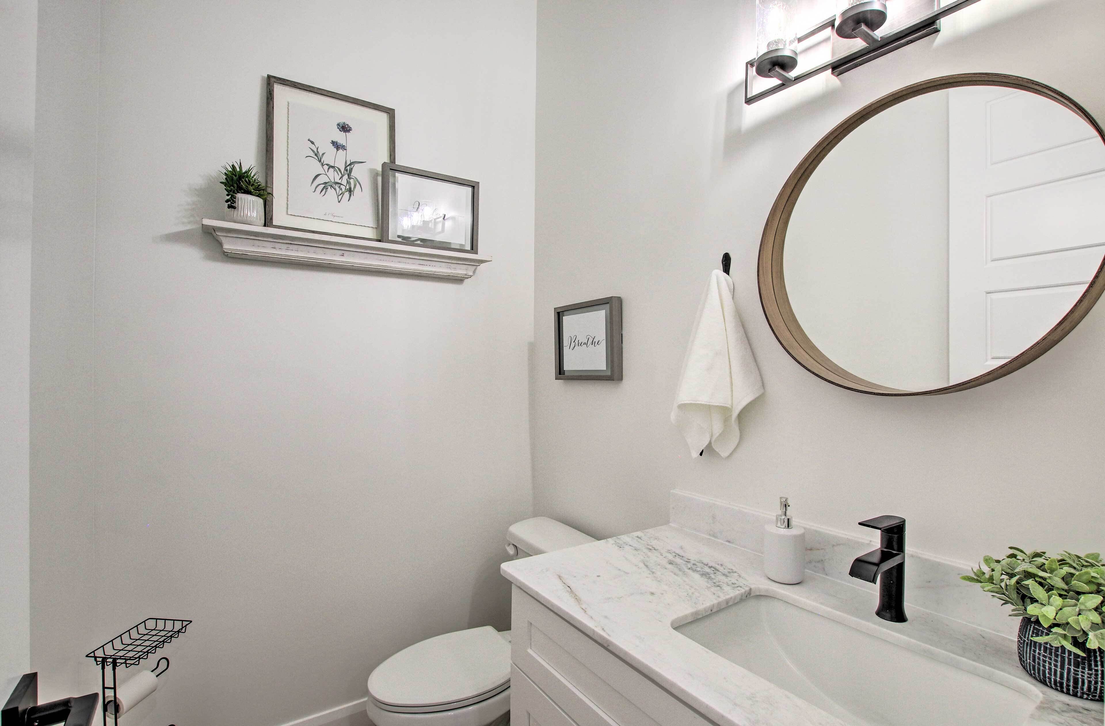 A bathroom with a toilet, sink, and mirror. There are framed pictures on the wall, a towel hanging on the wall, and a plant on the sink.