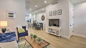 A modern living room with a sofa, coffee table, and TV stand. There is a dining area with a table and chairs, and a kitchen in the background. - Modern Mountain Escape Near Slopes, Lakes & Trails (Eden)