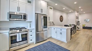 A modern kitchen with white cabinets, stainless steel appliances, and a dining area with a wooden table and chairs. - Modern Mountain Escape Near Slopes, Lakes & Trails (Eden)