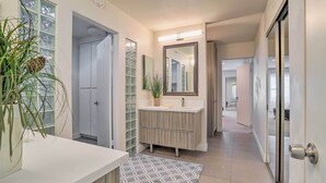 A modern bathroom with a white vanity, a large mirror, and a potted plant. - Sleek Rancho Mirage Villa: Patio, Pool, Golf! (Rancho Mirage)