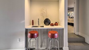 A compact kitchen with a white countertop, two red stools, and a decorative vase. - Sleek Rancho Mirage Villa: Patio, Pool, Golf! (Rancho Mirage)