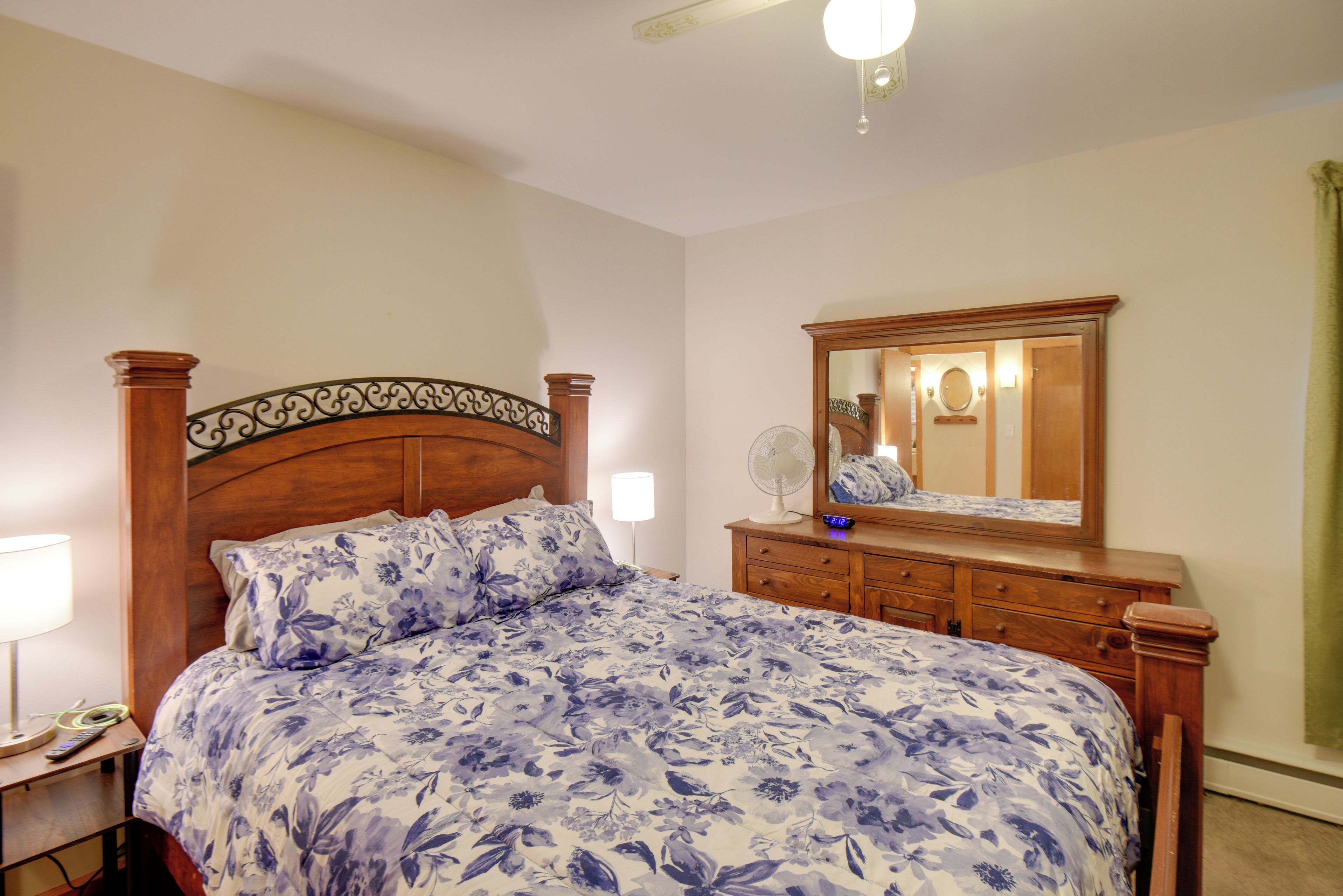 A bedroom with a wooden bed, a dresser, a mirror, and a bedside lamp.