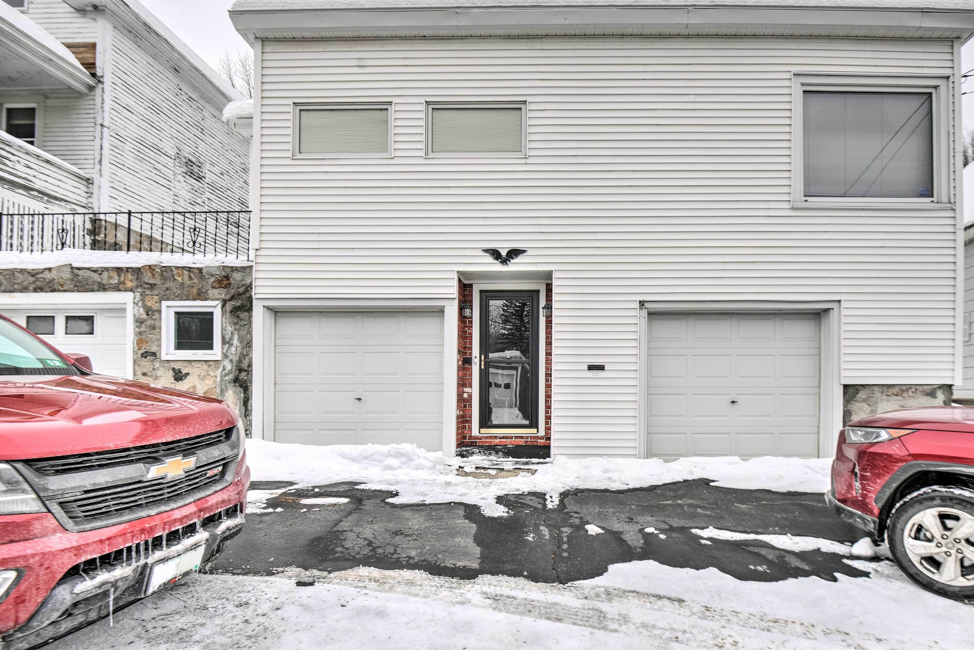 A two-story residential building with a garage, a front door with a decorative bird, and a driveway with snow.
