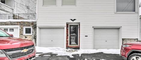 A two-story residential building with a garage, a front door with a decorative bird, and a driveway with snow.