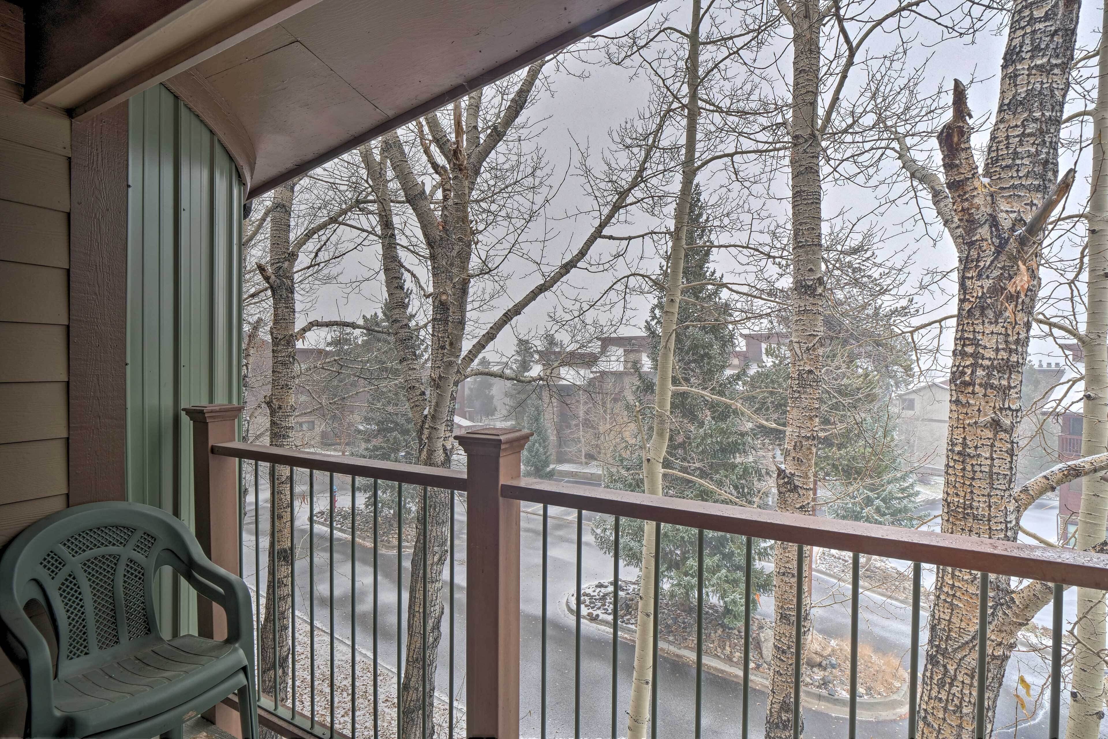 Un balcon avec une balustrade en métal, une chaise en plastique verte et une vue sur des arbres et une route.