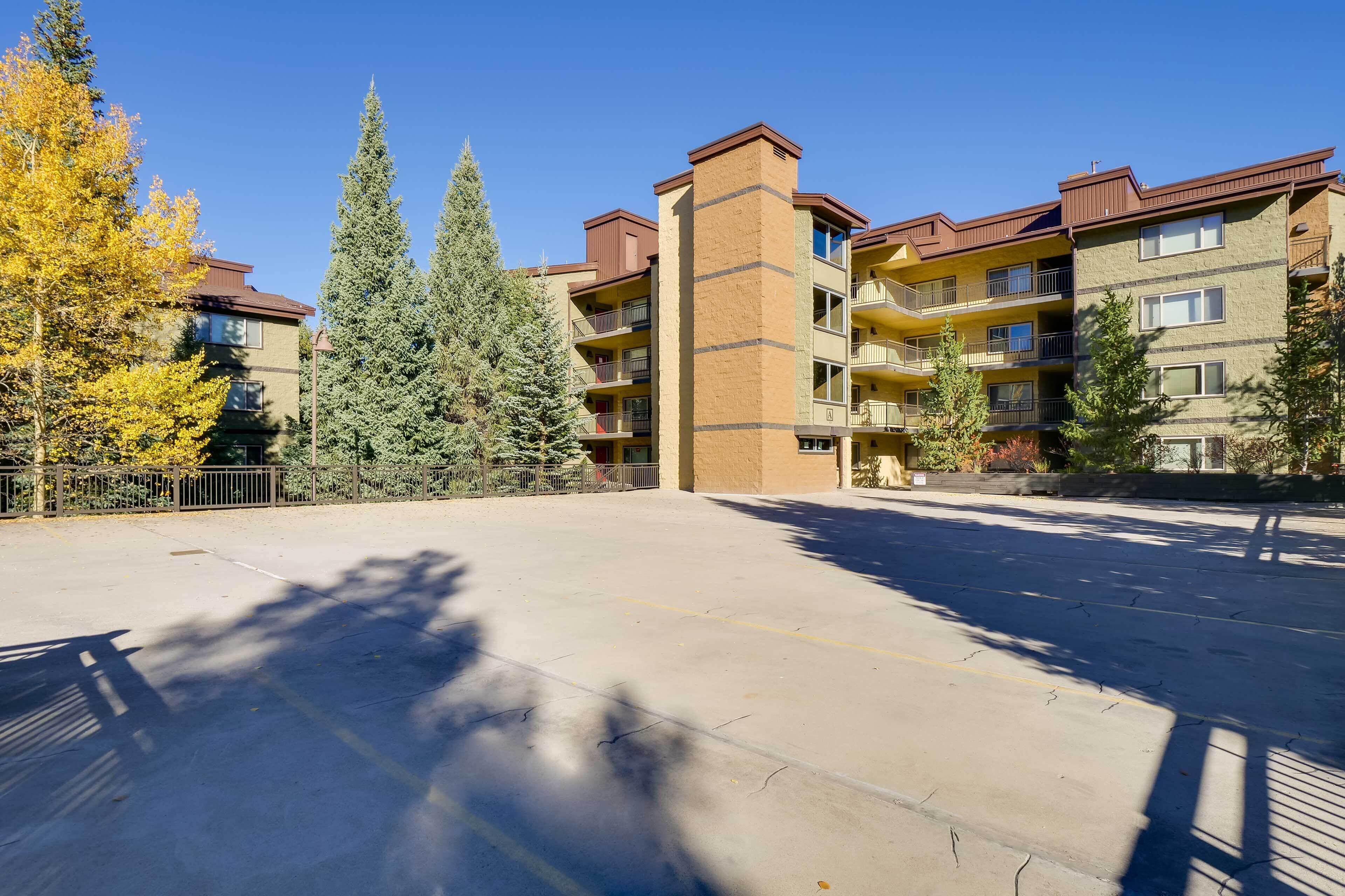 Un edificio residenziale a più piani con balconi, un parcheggio e alberi circostanti.
