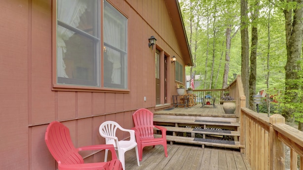 Eine Holzterrasse mit Adirondack-Stühlen, einem kleinen Tisch und Blick auf den Wald.