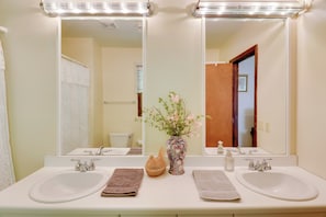 A bathroom with two sinks, a mirror, and a vase with flowers.