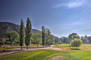 Um campo de golfe com céu claro, grama verde e árvores.