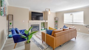 Een moderne woonkamer met een bank, een televisie, een open haard en een groot raam.