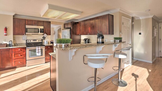 Een moderne keuken met houten kasten, roestvrijstalen apparatuur, een centraal eiland met barkrukken en een zichtbare brandblusser.