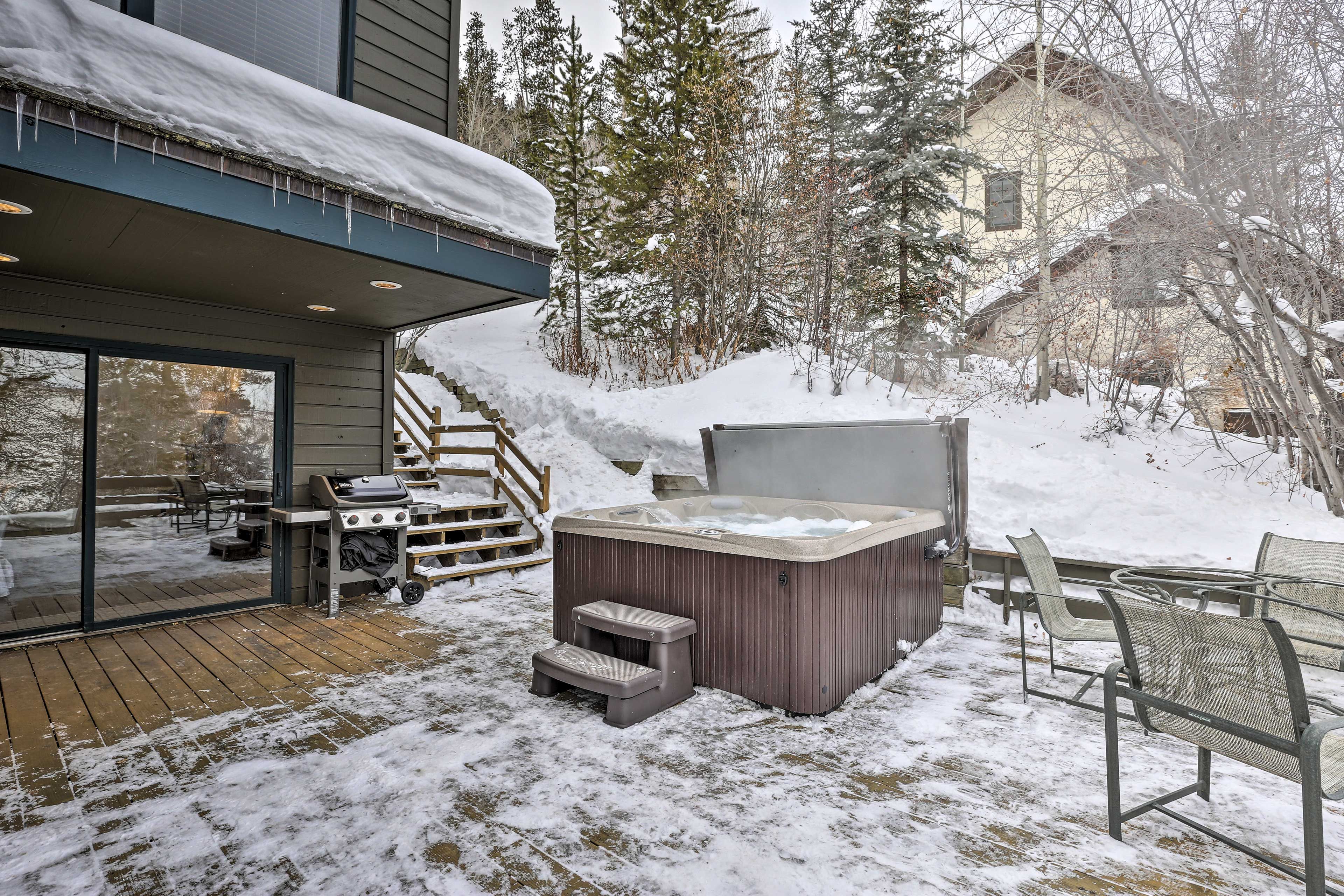 A hot tub and outdoor seating area with a wooden deck and steps leading to a glass door.